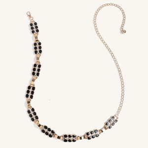 Détail de la chaîne de taille dorée avec trèfles noirs et strass scintillants sur fond blanc