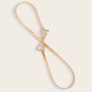 Détail d'une ceinture dorée élastique avec boucle en forme de nœud sertie de strass
