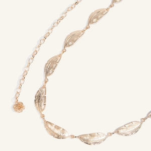 Detailed close-up of bohemian gold feather waist chain with a carved rose pendant