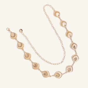 Macro detail of gold sea shell belt featuring polished metal charms and lobster clasp