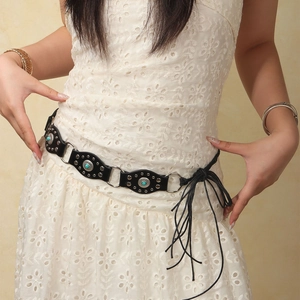 Détail d'une ceinture bohème noire avec pierres turquoise et longues franges sur dentelle