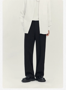 Dettaglio dei pantaloni neri a gamba dritta con drappeggio elegante e design minimalista