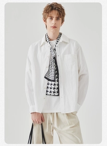 Detail of a minimalist black and white houndstooth scarf on a white long-sleeve shirt