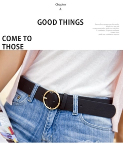 Detail of a dark brown leather belt with a round gold buckle on blue jeans and pink cardigan