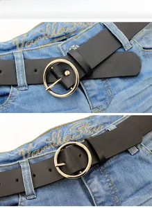 Detailed view of a black leather belt with a round gold buckle on blue denim jeans