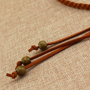 Vintage brown woven leather belt for women with wooden beads over rustic fabric background