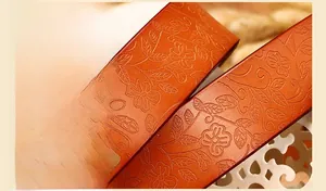Detail of orange-brown cowhide leather belt with intricate floral embossed patterns