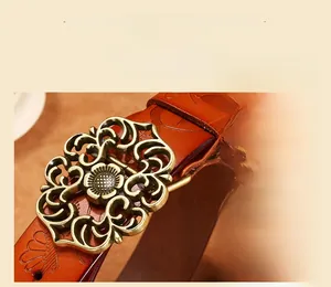 Gros plan de la boucle à fleurs en bronze vintage et motifs gaufrés sur ceinture en cuir brun