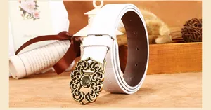 Détail d'une ceinture en cuir blanc montrant la boucle florale en bronze et les motifs embossés