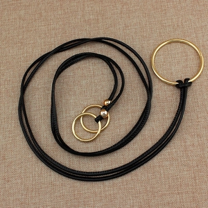 Collier minimaliste en cordon noir avec trois anneaux dorés sur tissu en jute brun
