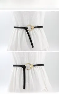 Détail d'une fine ceinture noire avec boucle ronde dorée nouée sur une robe fleurie