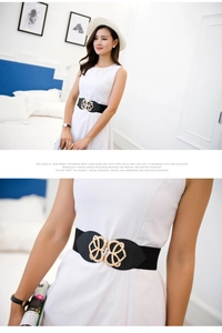 Detail view of wide elastic belt featuring gold heart buckle on elegant black dress