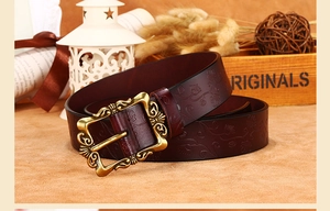 Détail de la ceinture en cuir marron rouge avec motif floral vintage et boucle bronze