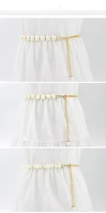 Détail de chaînes de taille dorées avec perles et breloques en nacre sur une robe blanche