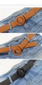 Vertical view of black and brown leather belts with round buckles on denim jeans