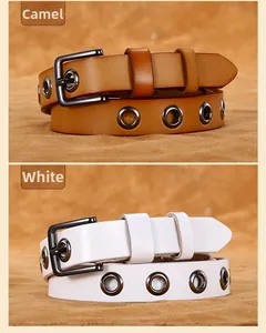 Dettaglio di cinture in pelle color cammello e bianco con occhielli su sabbia materica