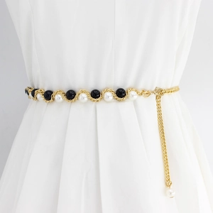 Détail d'une chaîne de taille dorée avec perles noires et blanches sur robe blanche