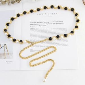 Détail d'une chaîne de taille dorée avec perles noires et blanches sur un magazine