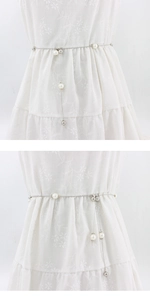 Detail showing elegant silver waist chain with pearls on a white embroidered dress