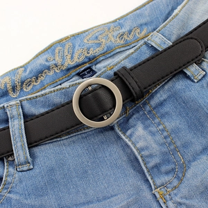 Ceinture fine en similicuir noir avec boucle ronde argentée sur un jean bleu denim