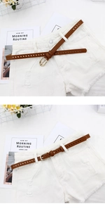 Detail of a thin brown leather belt with gold buckle styled on white distressed denim shorts