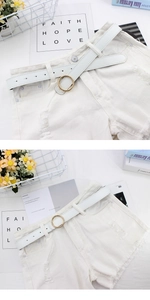 Détail d'une ceinture blanche à boucle ronde dorée sur un short en jean blanc
