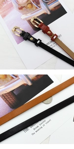 Dettaglio di cinture sottili in pelle nera e marrone con fibbie dorate lucide