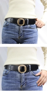 Détail d'une ceinture en cuir noir avec boucle ronde dorée mate sur un jean et un pull crème