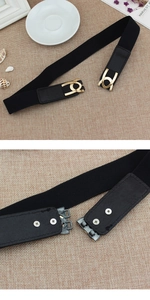 Detailed macro view of the black elastic waist belt with gold interlocking metal buckle