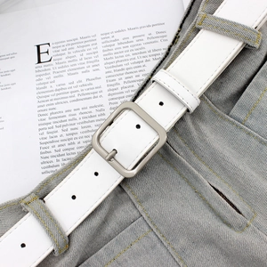Ceinture élégante en similicuir blanc avec boucle carrée mate sur un pantalon gris