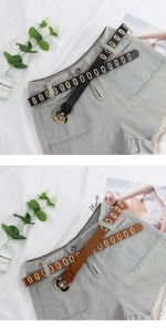 Detail of black and brown leather belts with golden oval eyelets on denim shorts