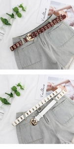 Detail view of thin leather belts with gold oval eyelets and round buckles on denim