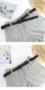 Detail of light blue denim shorts featuring a thin black leather belt with a golden round buckle