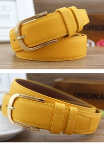 Detail of yellow faux leather skinny belt with golden D-ring buckle on wooden table