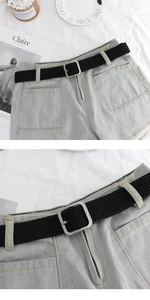 Detail of a black woven elastic belt with a square matte metal buckle on blue denim shorts