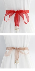 Detail of red and champagne ribbon belts with pearl pendants and delicate stitching