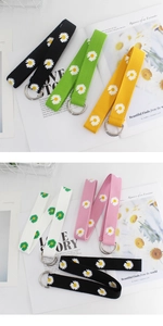 Detail of colorful canvas belts featuring daisy floral embroidery and metallic D-ring buckles