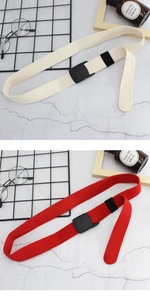 Détail de ceintures en toile rouge et crème avec boucles en plastique noir mat sur fond gris