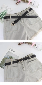 Dettaglio di pantaloncini di jeans con orli sfrangiati e sottile cintura in pelle nera con fibbia oro
