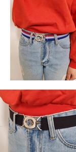 Detail of adjustable elastic belts with round interlocking metal buckle on denim jeans
