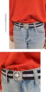 Detail of elastic black and white striped belt with a silver flower buckle on jeans