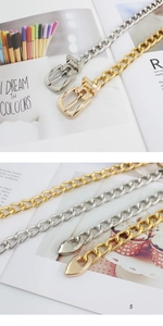 Detail of hollow metal chain belt with D-buckle and heart pendant in gold and silver