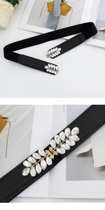 Detail of elegant leaf-shaped crystal buckle on a black elastic waist belt for women
