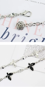 Detail of silver metal chain with black enamel butterfly, rose charm and rhinestone