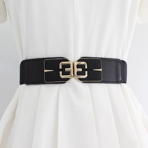 Women's black elastic waist belt with geometric gold buckle on a white dress