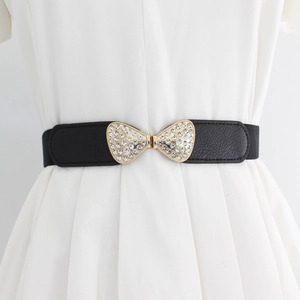 Women's vintage black elastic belt with a golden rhinestone bow buckle on white dress