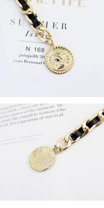 Detail of gold metal chain with black leather weaving and embossed coin pendant