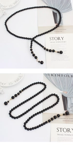 Détail de la ceinture en perles noires avec accents dorés et pendentif sur plateau
