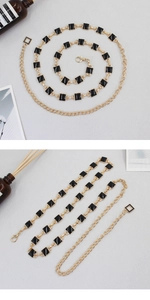 Detail of golden metal waist chain with black enamel square charms and lobster clasp