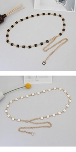 Detail view of gold alloy waist chains with black and white square inserts and adjustable links
